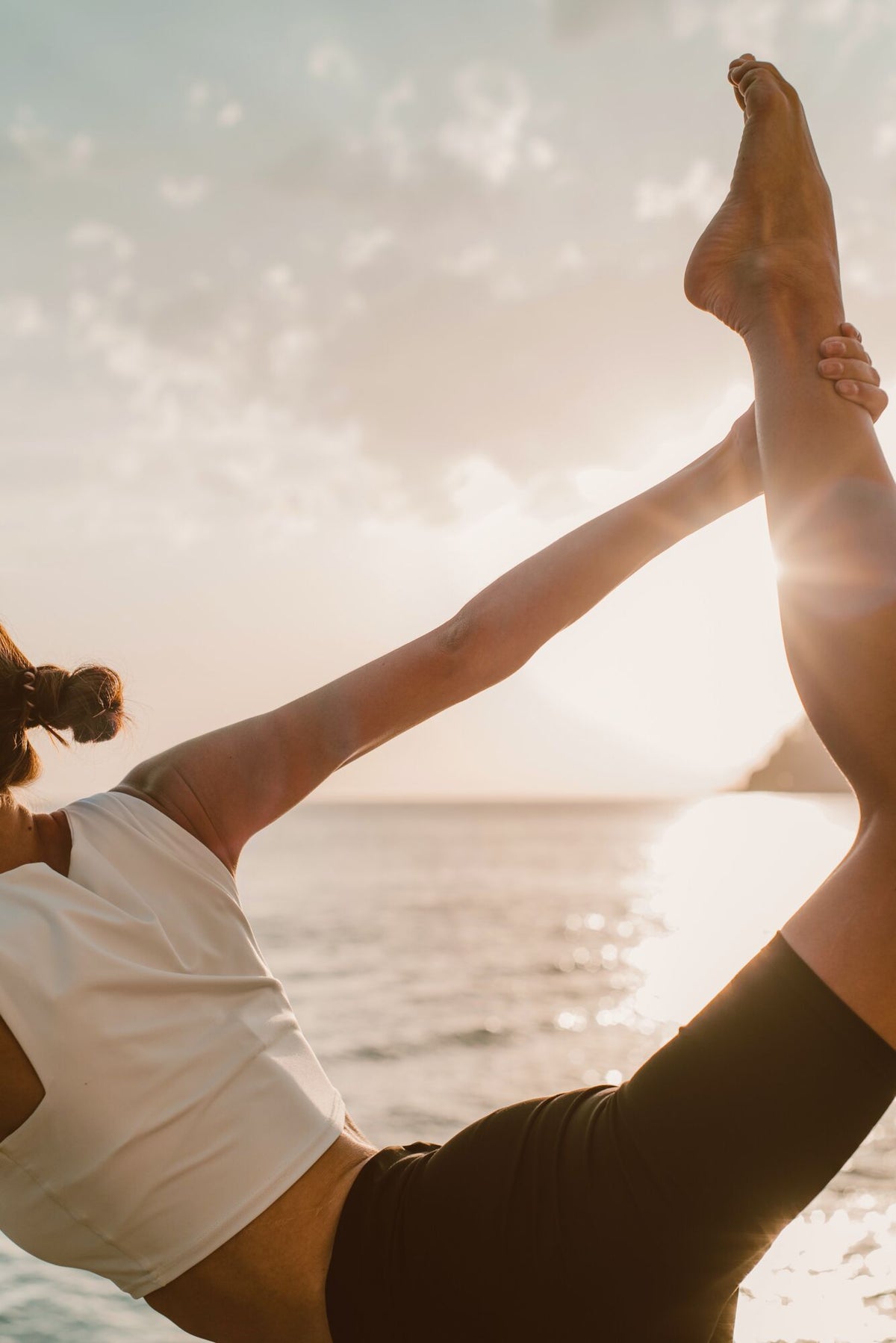 Frau in Yogapose am Strand beim Sonnenuntergang