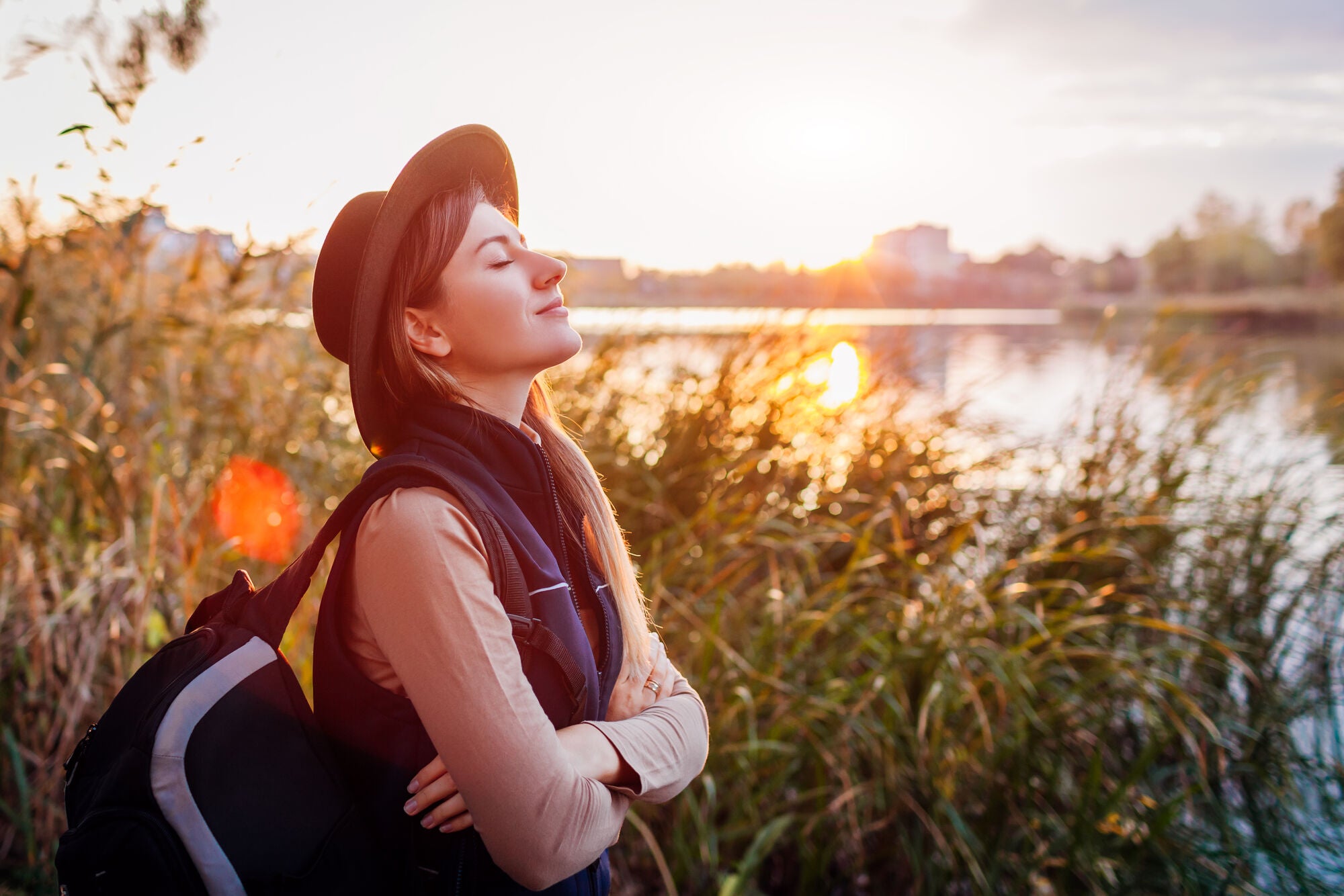 Frau steht entspannt im Sonnenuntergang am See